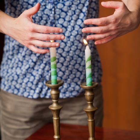 two shabbat candles are lit as someone's hands wave in the light of Shabbat
