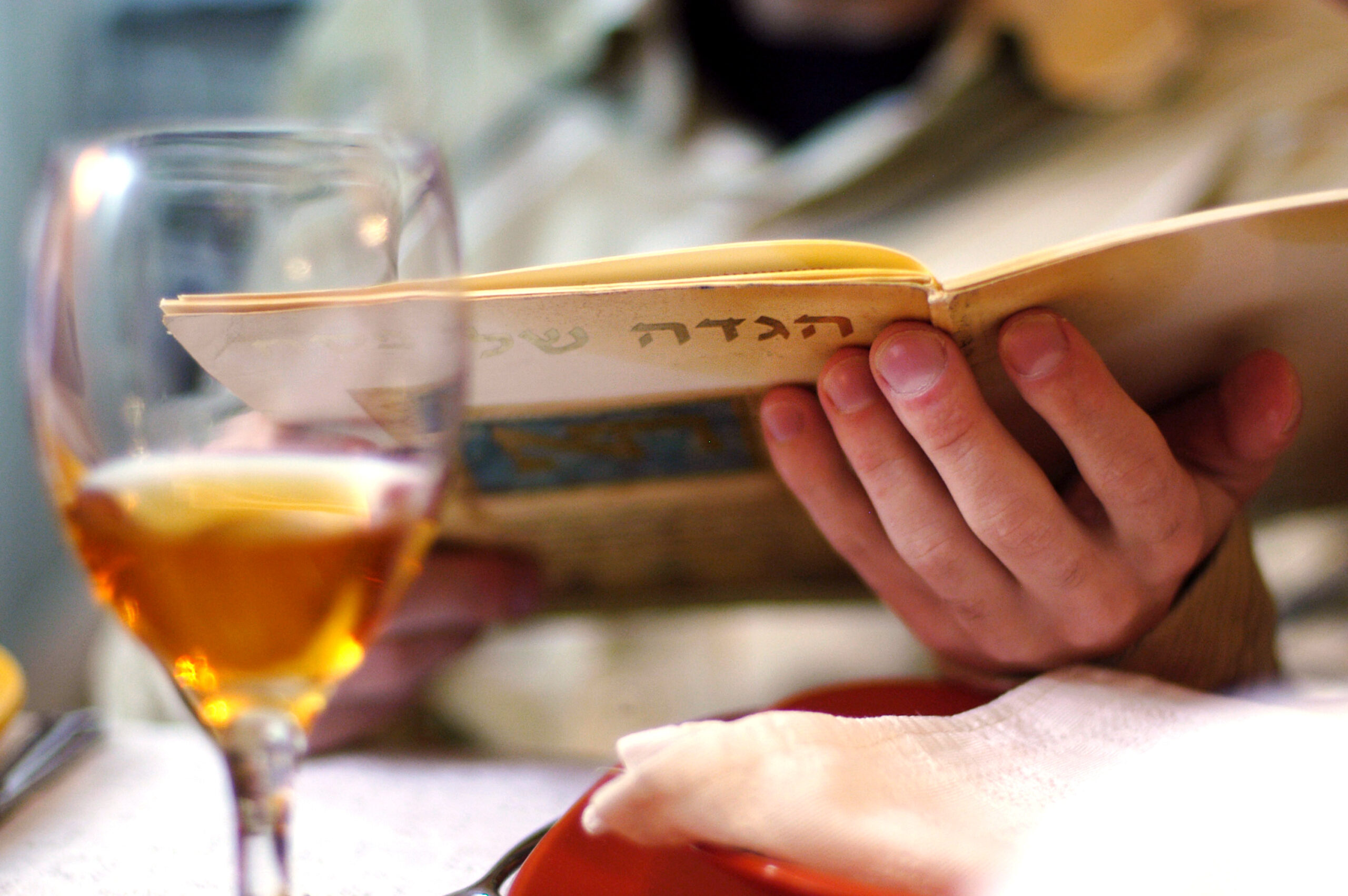 a wine glass and the hand of someone holding a Haggadah