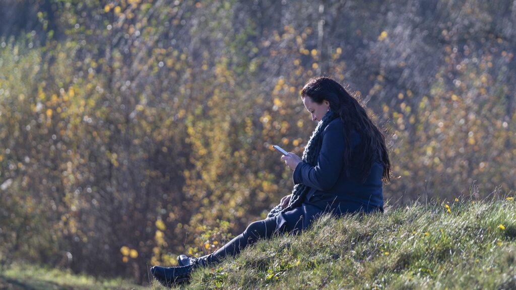 a woman sits on the grass looking at her phone