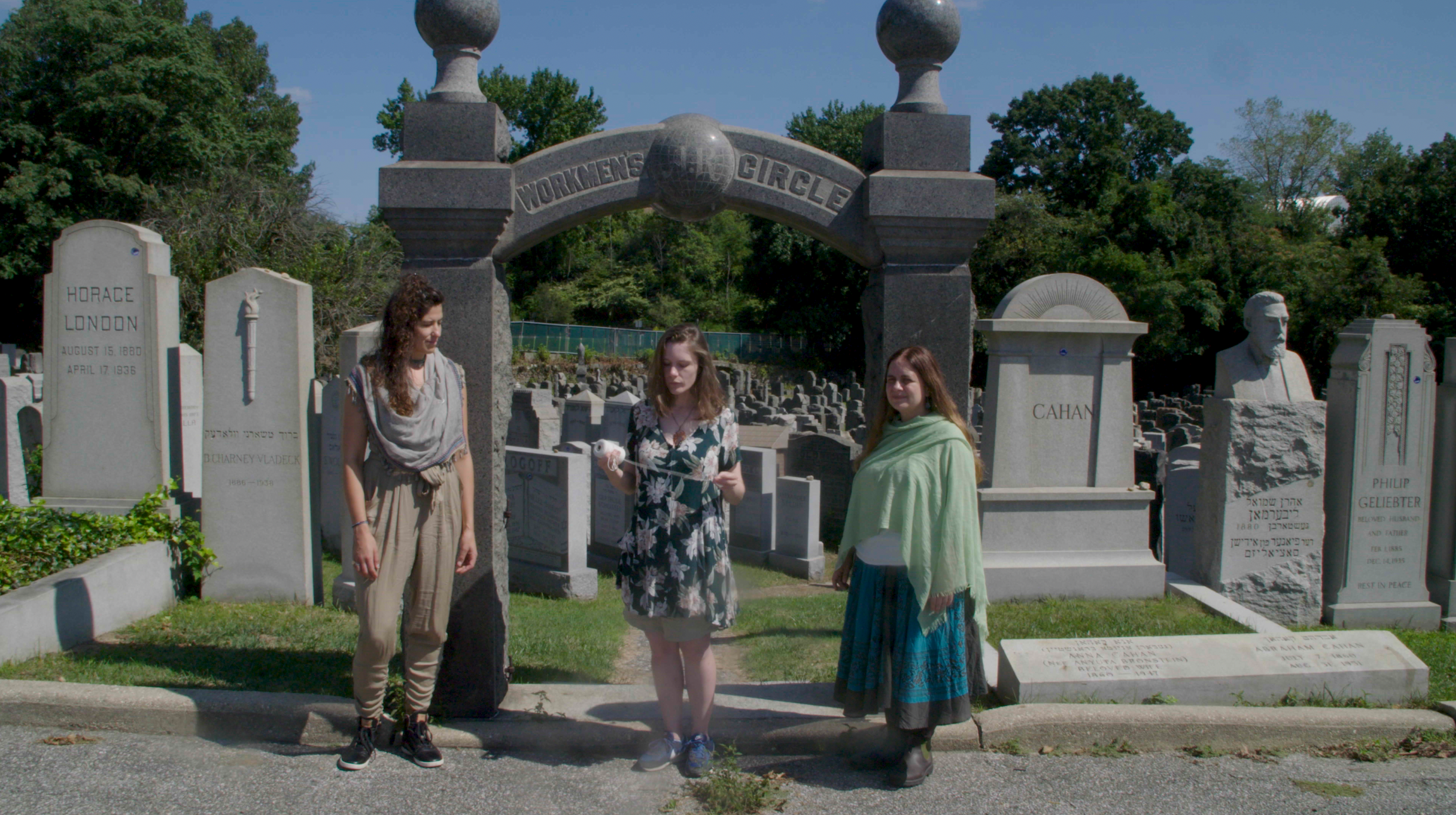 Three women stand at the gate of a cemetery