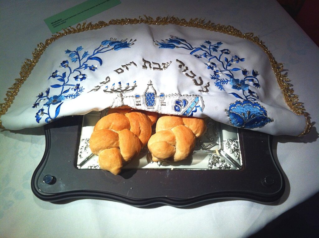 two braided challah under a white and blue cover