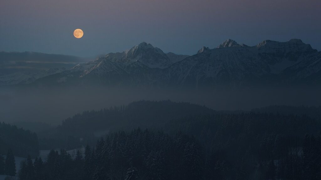 a full moon over mountains at twilight