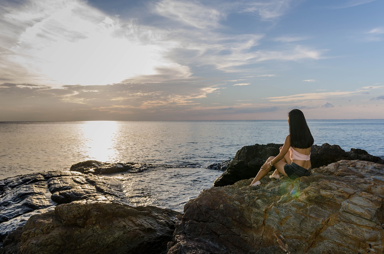 a person sitting on a large rock looking into the sea
