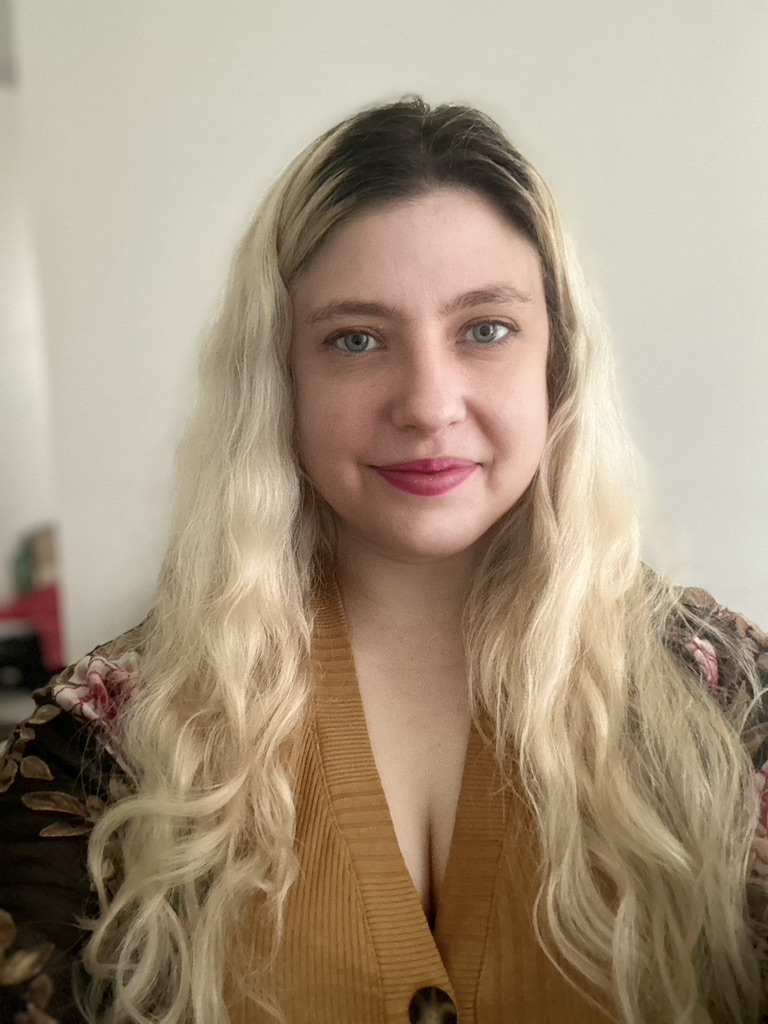 a woman is pictured with long blond hair with dark roots and a slight smile