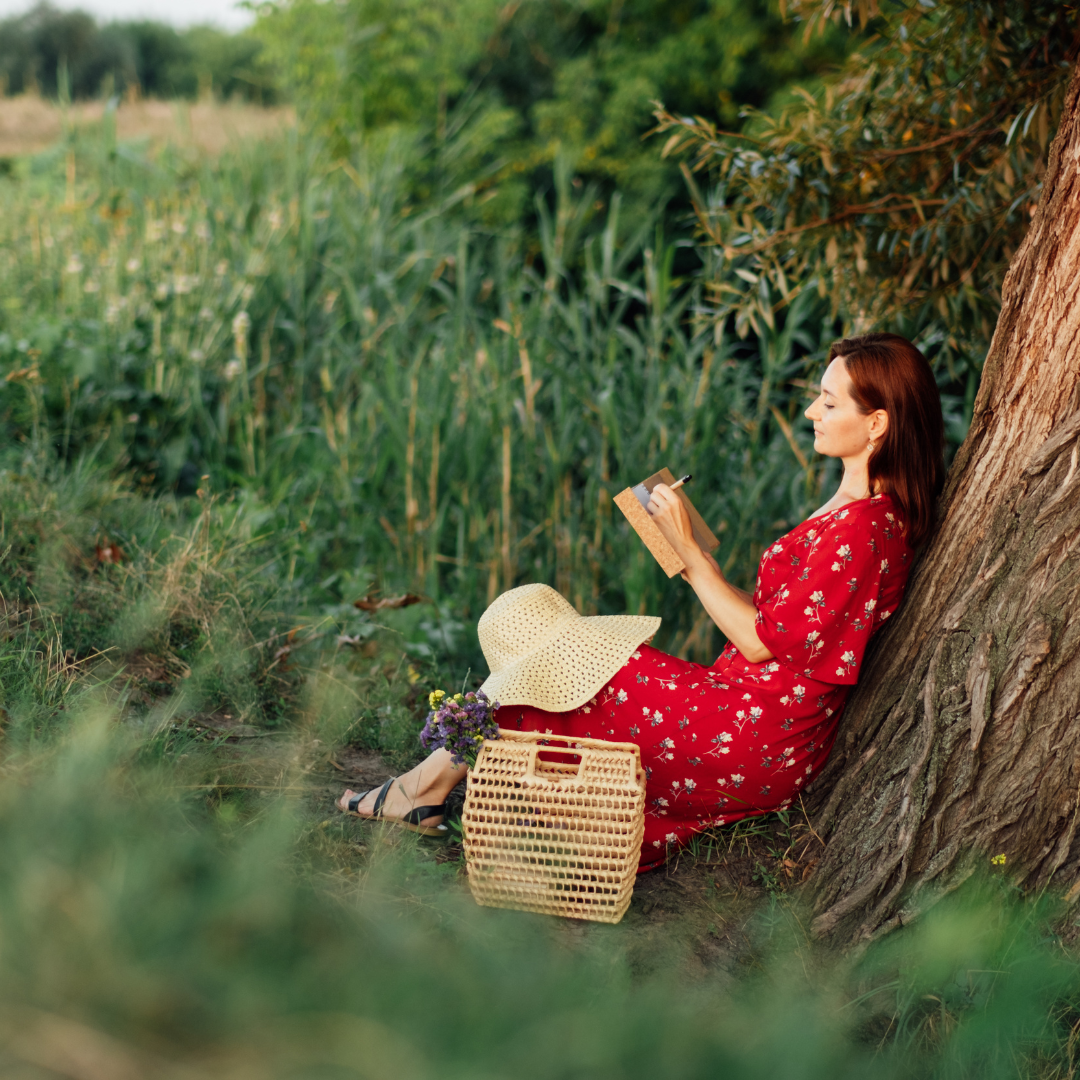 a woman sits under a tree with a journal