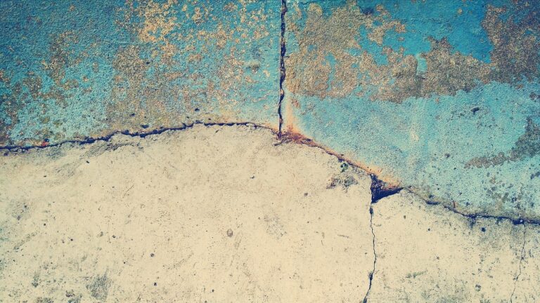a close=up of cracks in a wall, the surface is blue in places and beige below