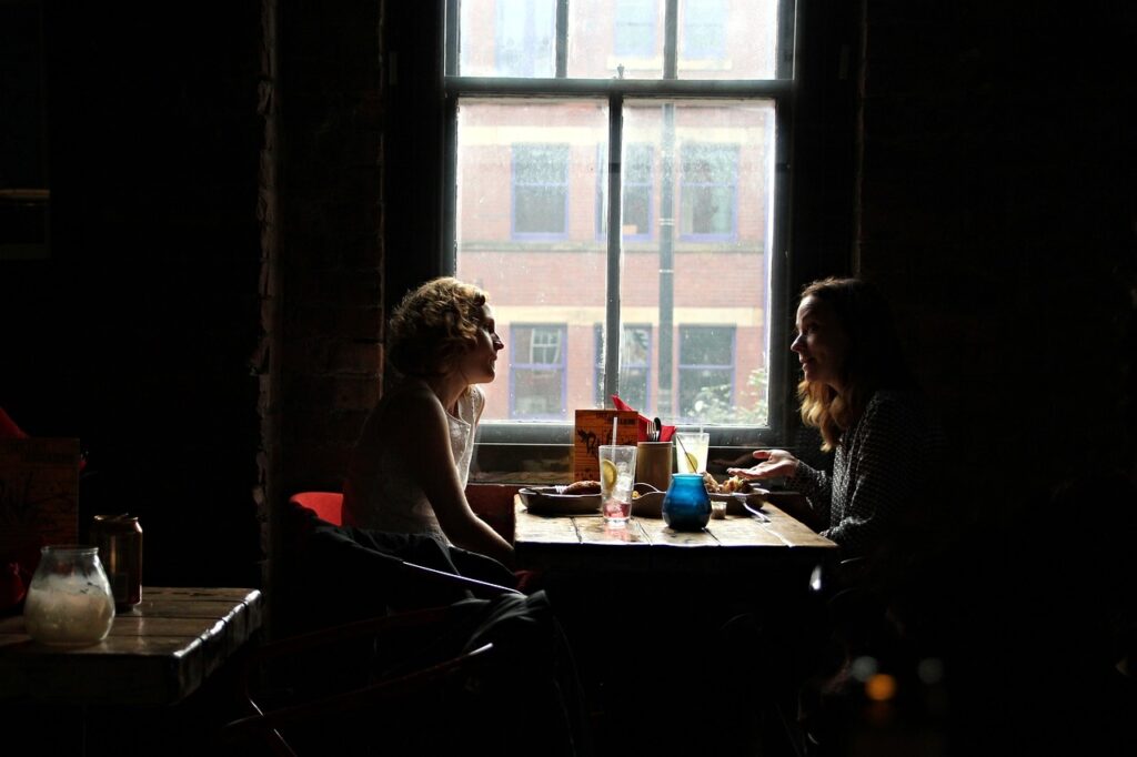 two women sit across from each other in a darkly lit restaurant, engaging in conversation