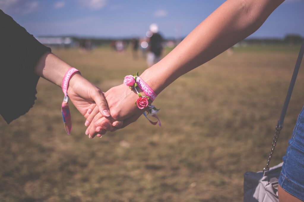 two people hold hands in a grassy field who are wearing identical pink wristbands that say "camping"