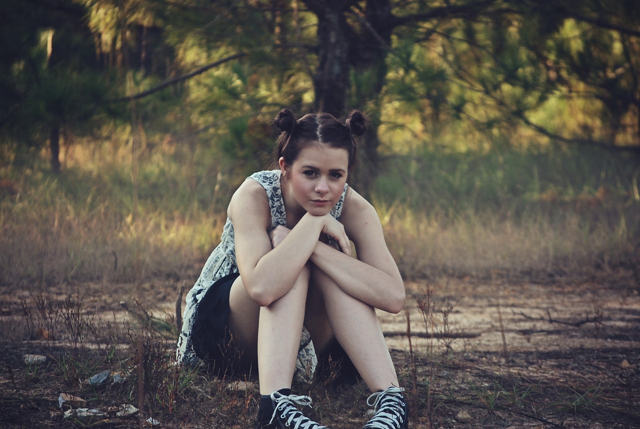 girl sitting outside, trees behind her