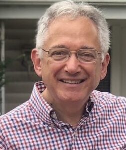 Rabbi Dan Liben has grey hair and glasses. He smiles at the camera 