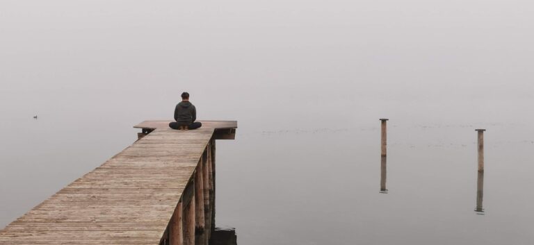 a person sitting at the end of a dock, looking into a lake