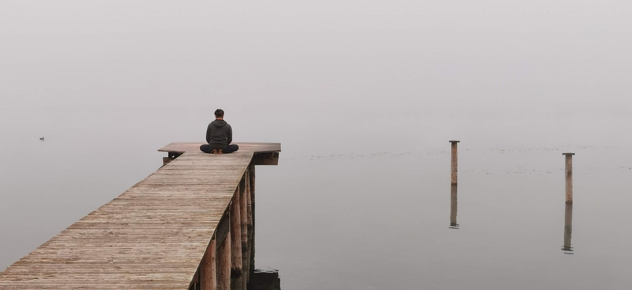 a person sitting at the end of a dock, looking into a lake