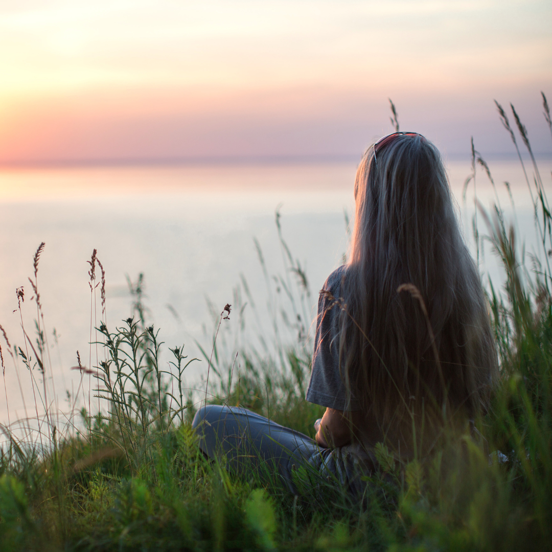 a woman sits and looks into the sunset over the water