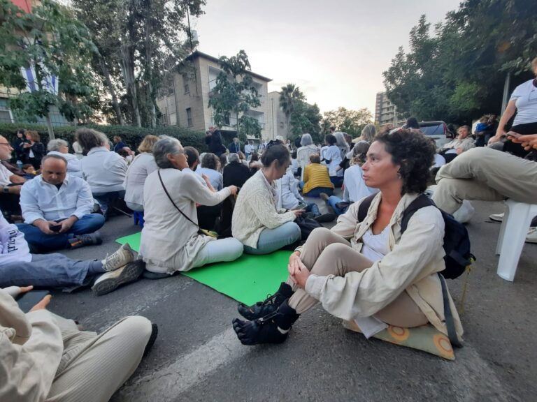 Rabbi Haviva dressed in white sits with protestors