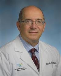 Dr. Barry Mann wears a white doctor's coat. He is a blading man wearing glasses.