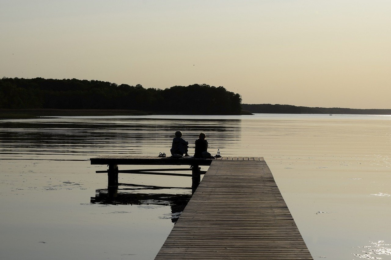 two people sit on a dock looking out over a lake