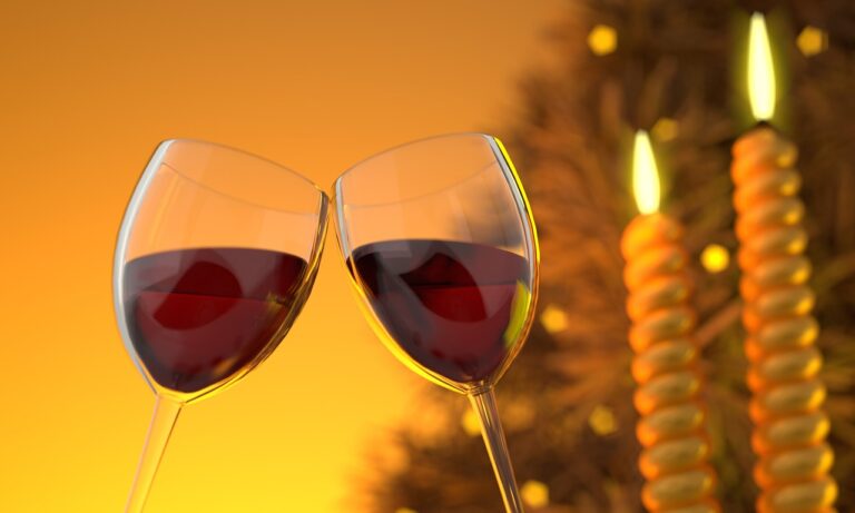 Two glasses of red wine clinking against a warm golden background with lit candles.