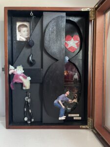 Shadow box with number 48, childhood photos, heart, puppet, and small hanging items.