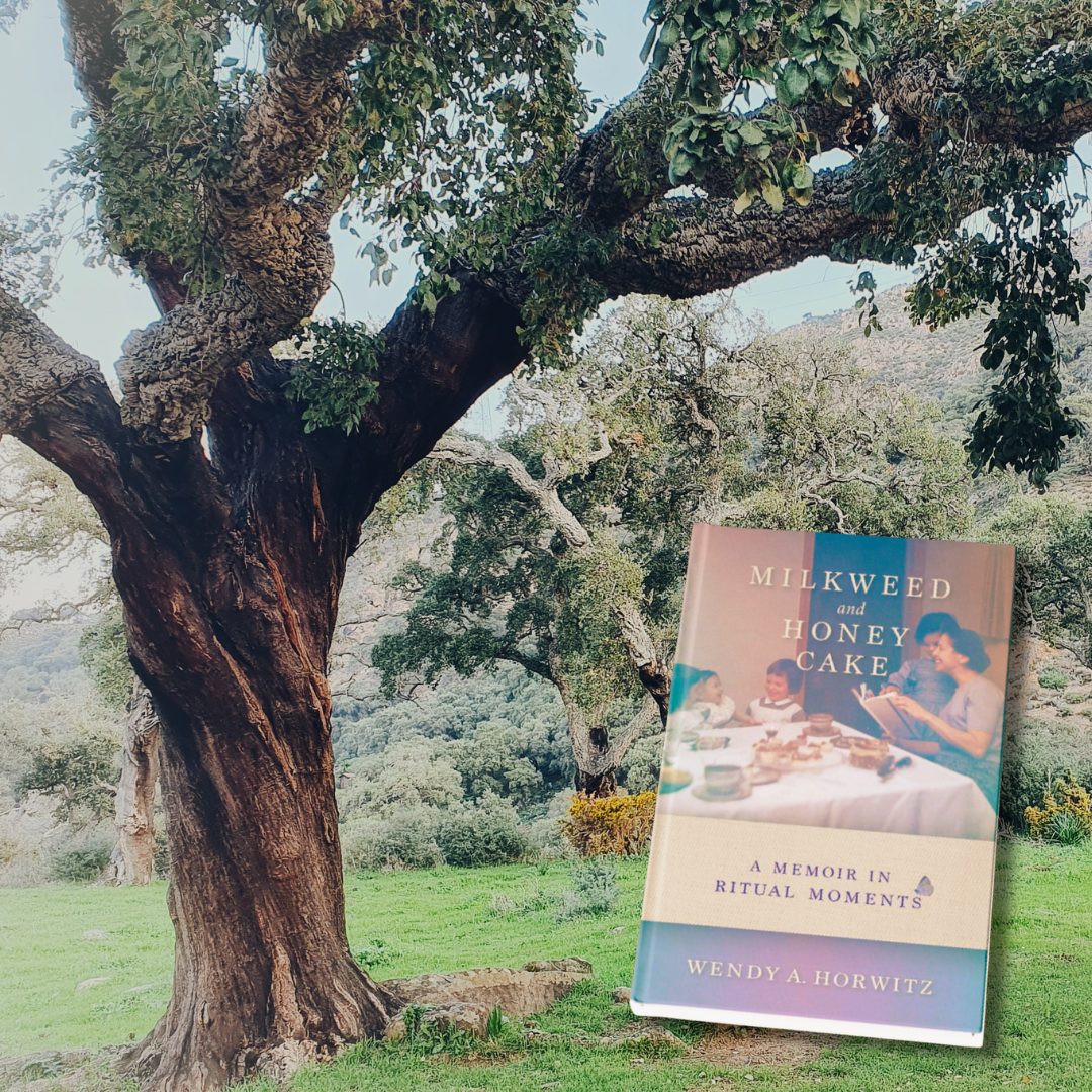 A book titled Milkweed and Honey Cake is displayed in front of a large tree and green landscape.