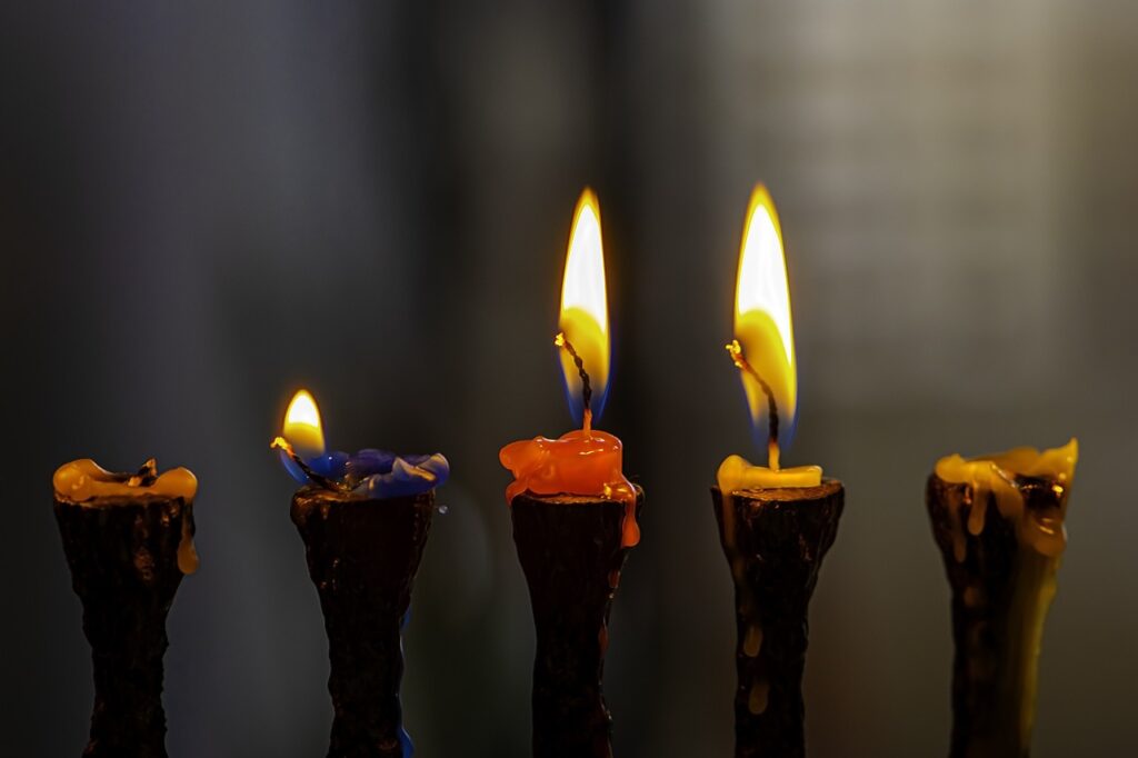 Four lit candles with blue, orange, and yellow wax dripping down, set against a dark, blurred background.