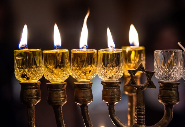 A menorah with six lit candles and detailed glass holders.