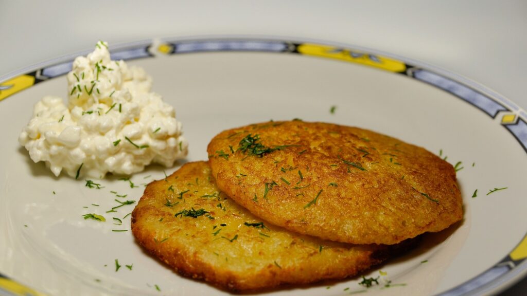 Two potato pancakes garnished with dill on a plate, served with a side of cottage cheese.