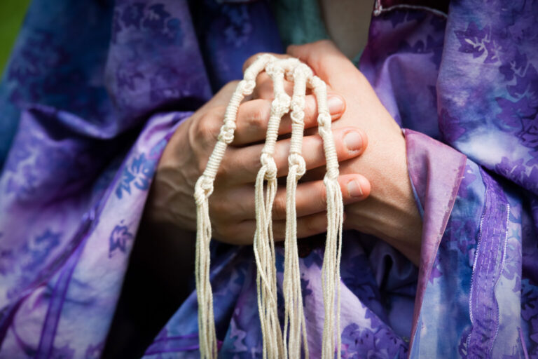 a person in a purple tallit gathers the four tzit-tzit in their hands