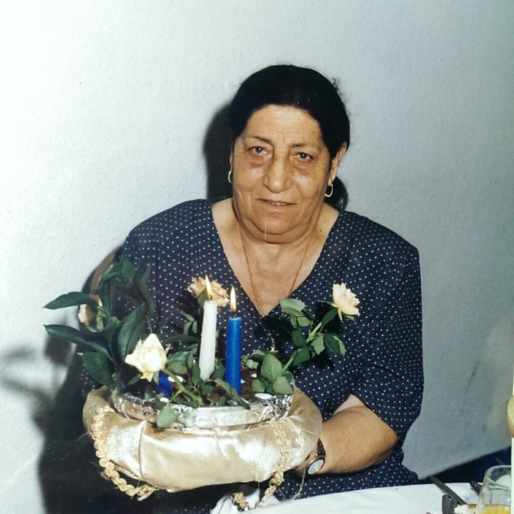 Elderly woman holding a floral arrangement with candles at a table.