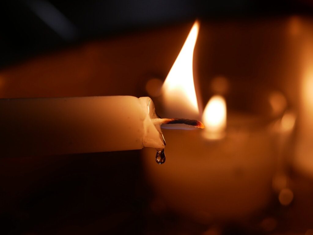 Close-up of a lit candle with a melting wax drip and soft flame in the background.