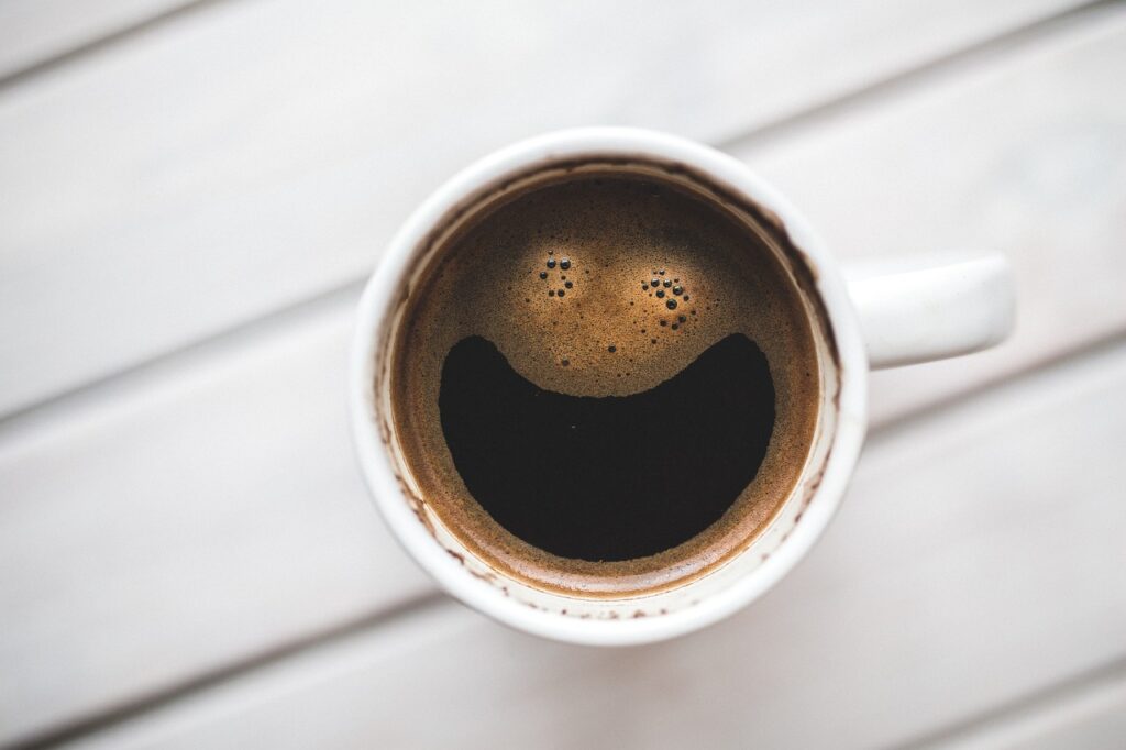 A cup of coffee with a smiling face pattern formed by bubbles on a wooden surface.