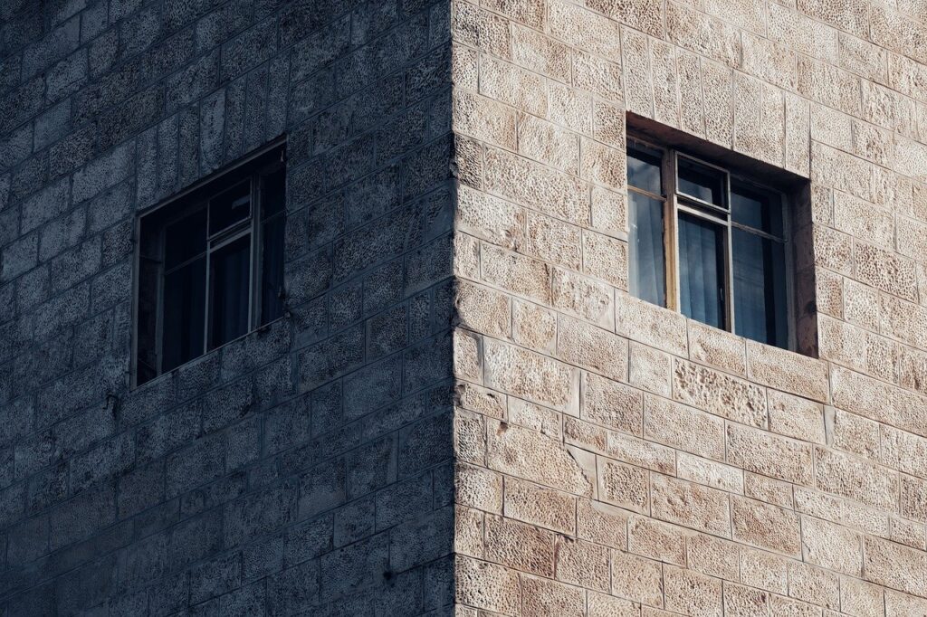 Corner of a stone building with two windows, featuring a textured, sunlit facade.