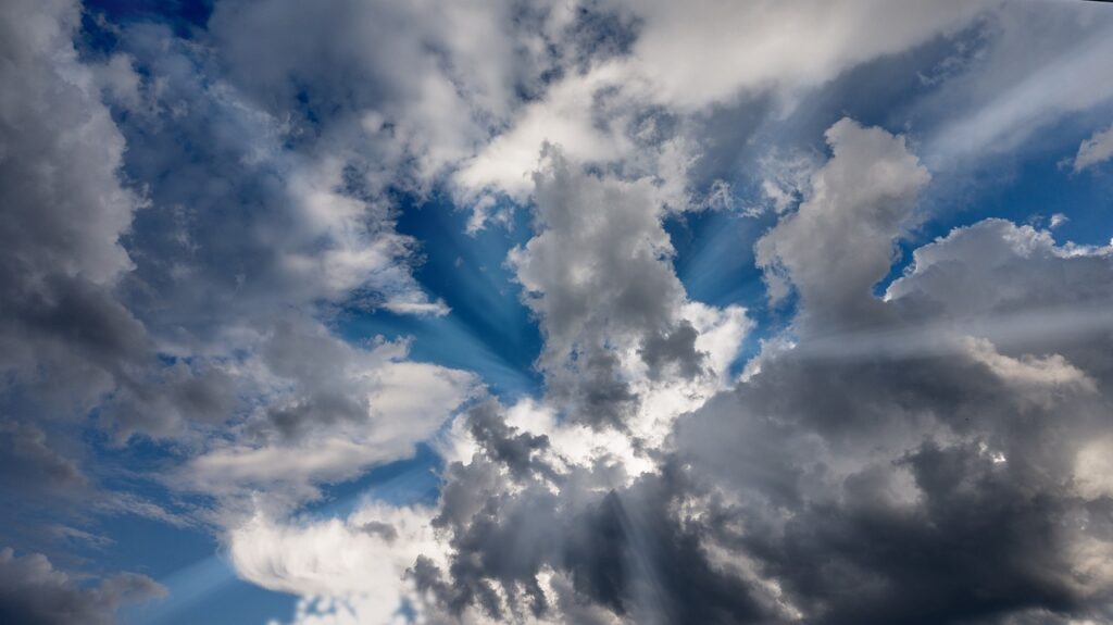 Dramatic sky with sunbeams breaking through fluffy, dark clouds against a vibrant blue backdrop.