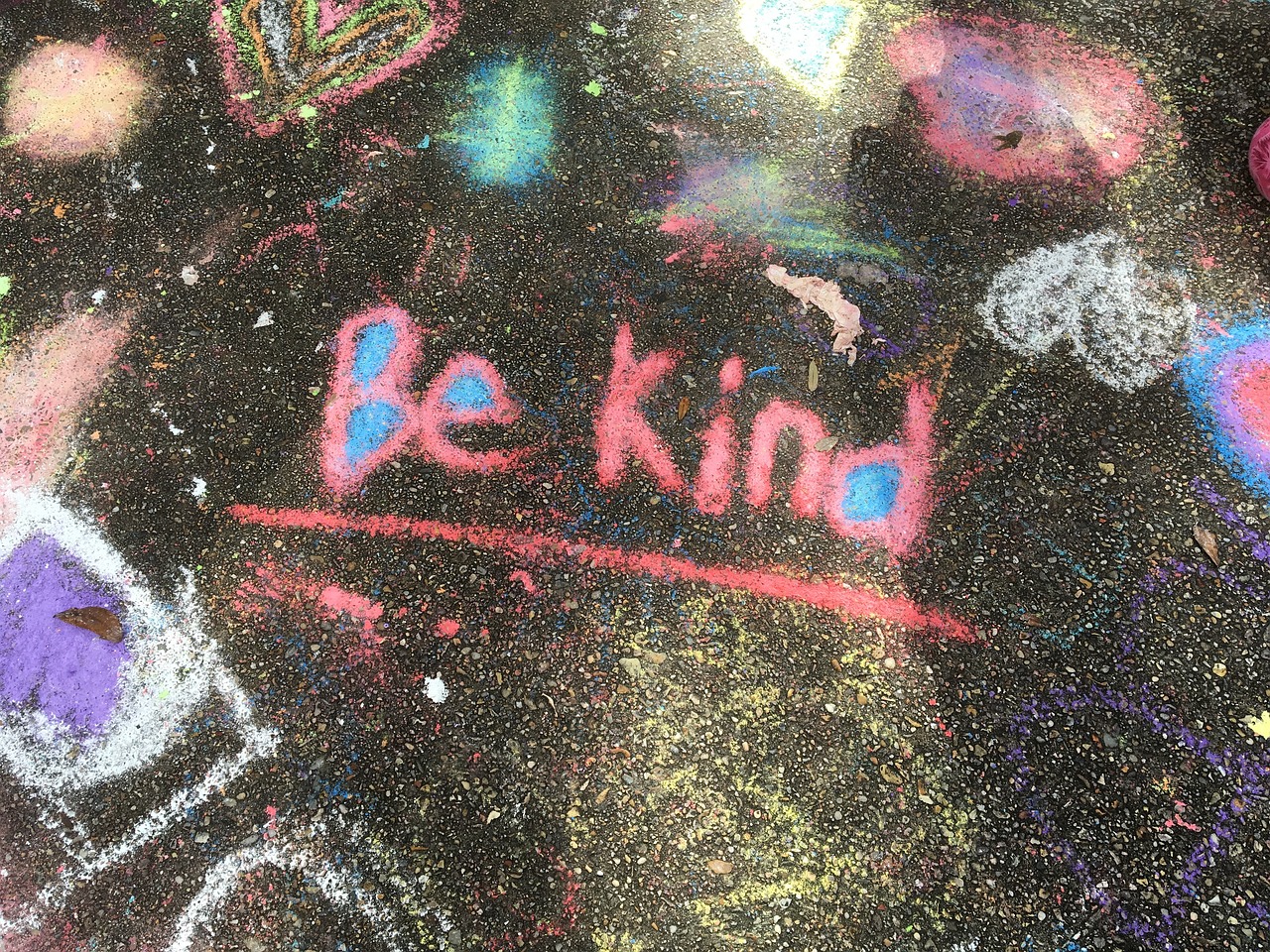 Colorful chalk drawing on pavement with the message Be Kind in pink and blue.