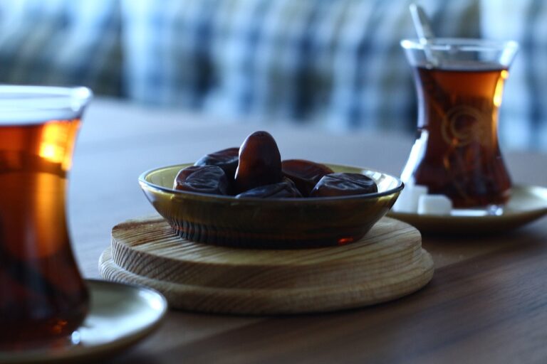 Glasses of tea next to a bowl of dates on a wooden table.