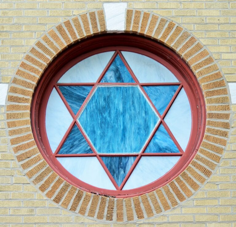 Circular stained glass window with a blue Star of David, set in a brick wall.