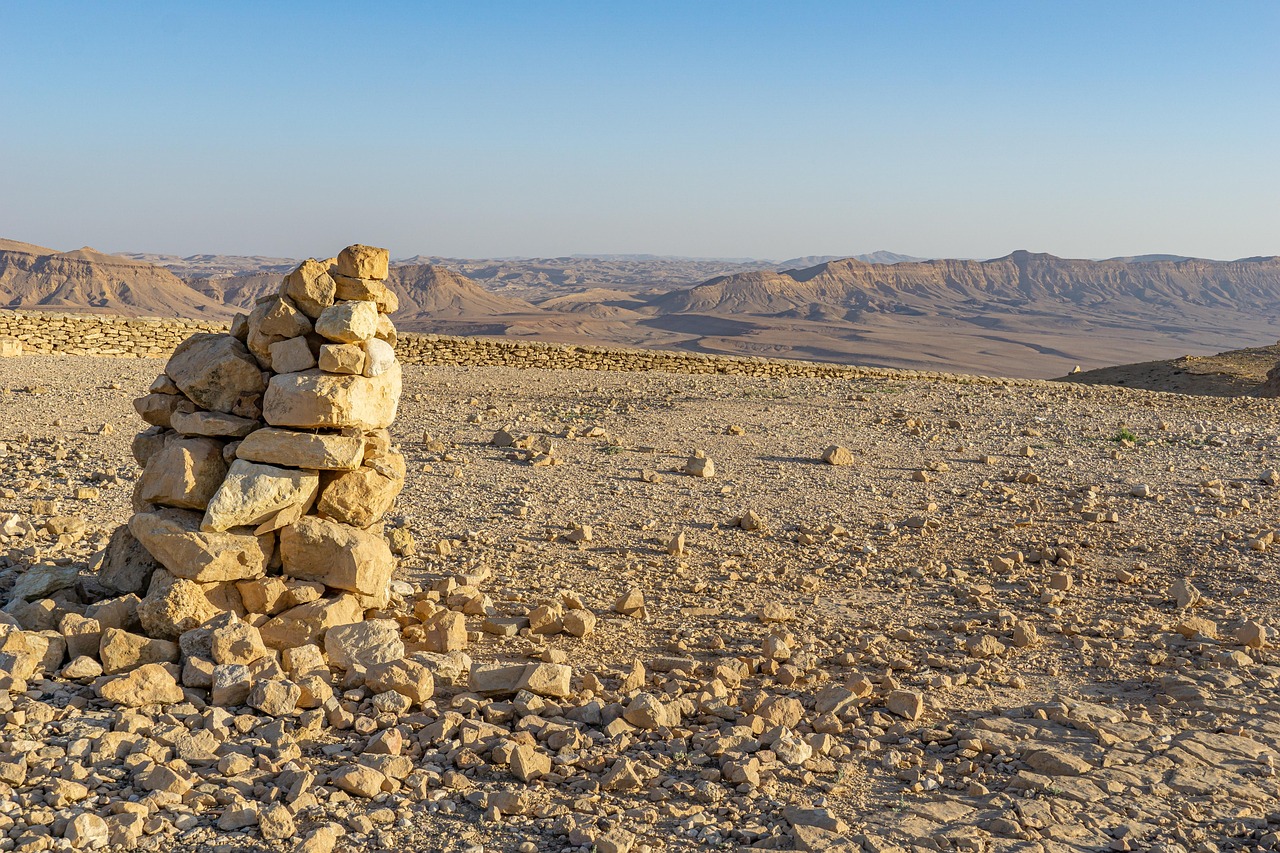 A stack of rocks on a desert landscape with distant mountains under a clear blue sky.