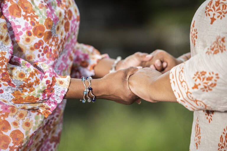 Two individuals in floral-patterned clothing holding hands outdoors, conveying a sense of support and connection.