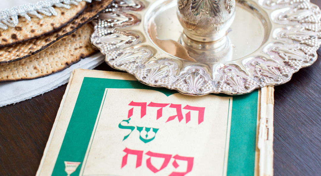 Passover arrangement with a Hebrew Haggadah, a decorative silver cup on a plate, and matzah.