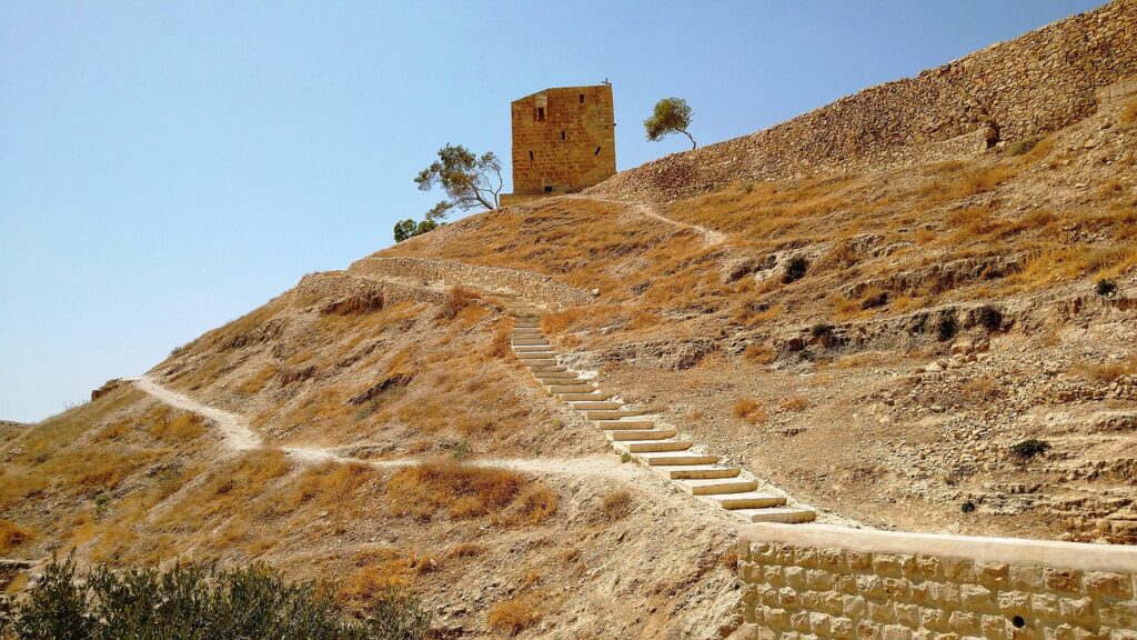 Stone stairway leading up a dry, rocky hill to a small building under a clear blue sky.