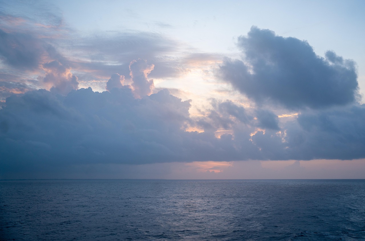 Calm ocean under a cloudy sky at sunset, with soft light illuminating the clouds and horizon.