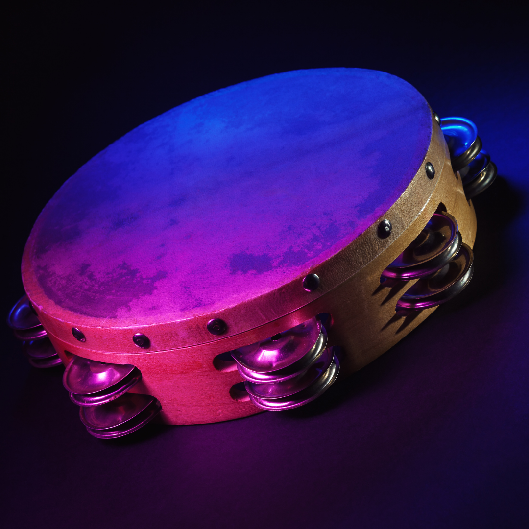 A tambourine with metal jingles is lit by purple and blue lights on a dark background.