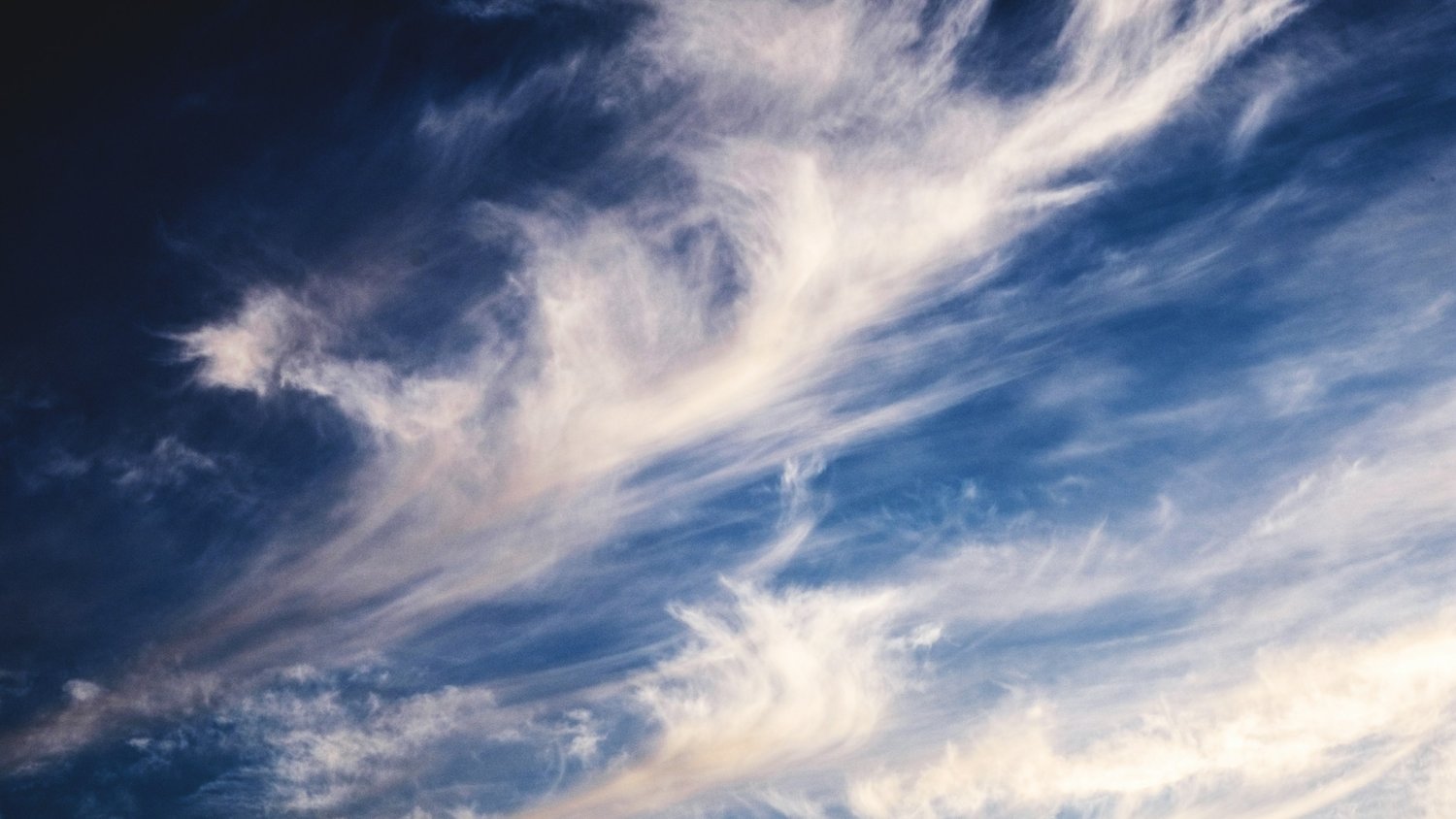Wispy white clouds stretch across a deep blue sky, creating a dynamic, airy pattern.