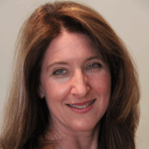 Woman with long brown hair and a friendly smile, posing in front of a plain light background.