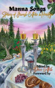 A colorful table with challah, grapes, wine, and two Shabbat candles set outdoors near a stream and trees.