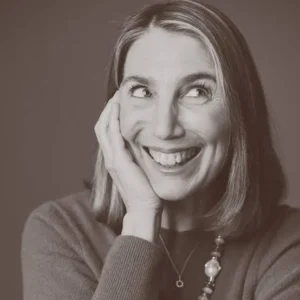 Smiling woman with chin in hand, looking up and to the side, in a black and white portrait.