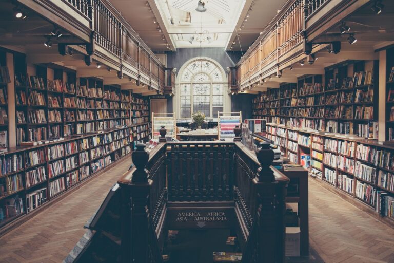 Old library interior with tall bookshelves, wooden railings, and a large arched window at the far end.