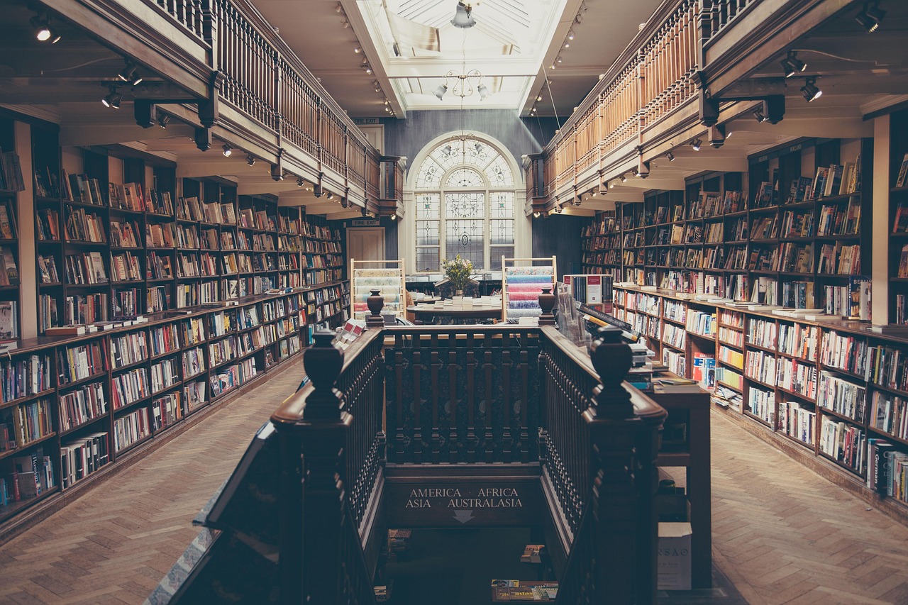 Old library interior with tall bookshelves, wooden railings, and a large arched window at the far end.