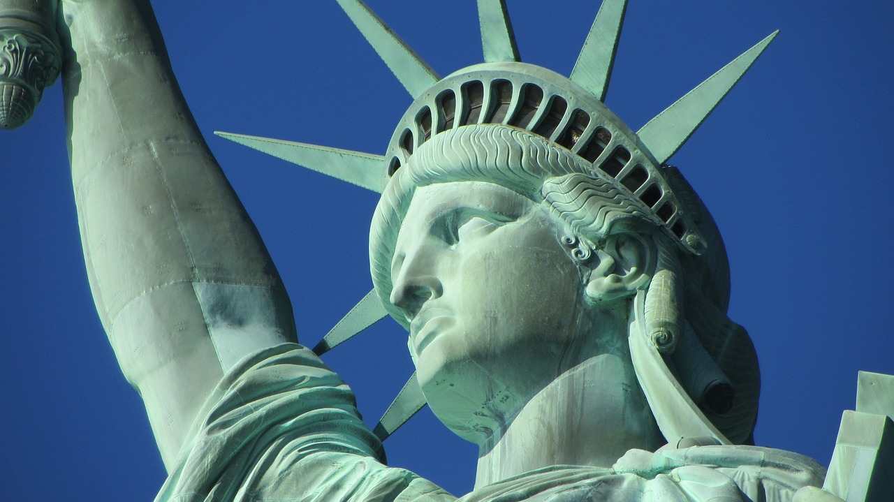 Close-up of the Statue of Liberty’s face and torch arm against a clear blue sky.