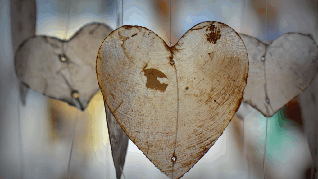 A close-up of heart-shaped wooden ornaments hanging on strings with a blurred background.