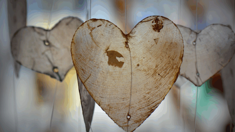 A close-up of heart-shaped wooden ornaments hanging on strings with a blurred background.